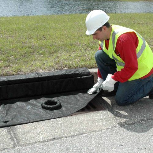 Worker laying an UltraTech Inlet Guard Plus magnetic storm drain filter over a curb inlet grate