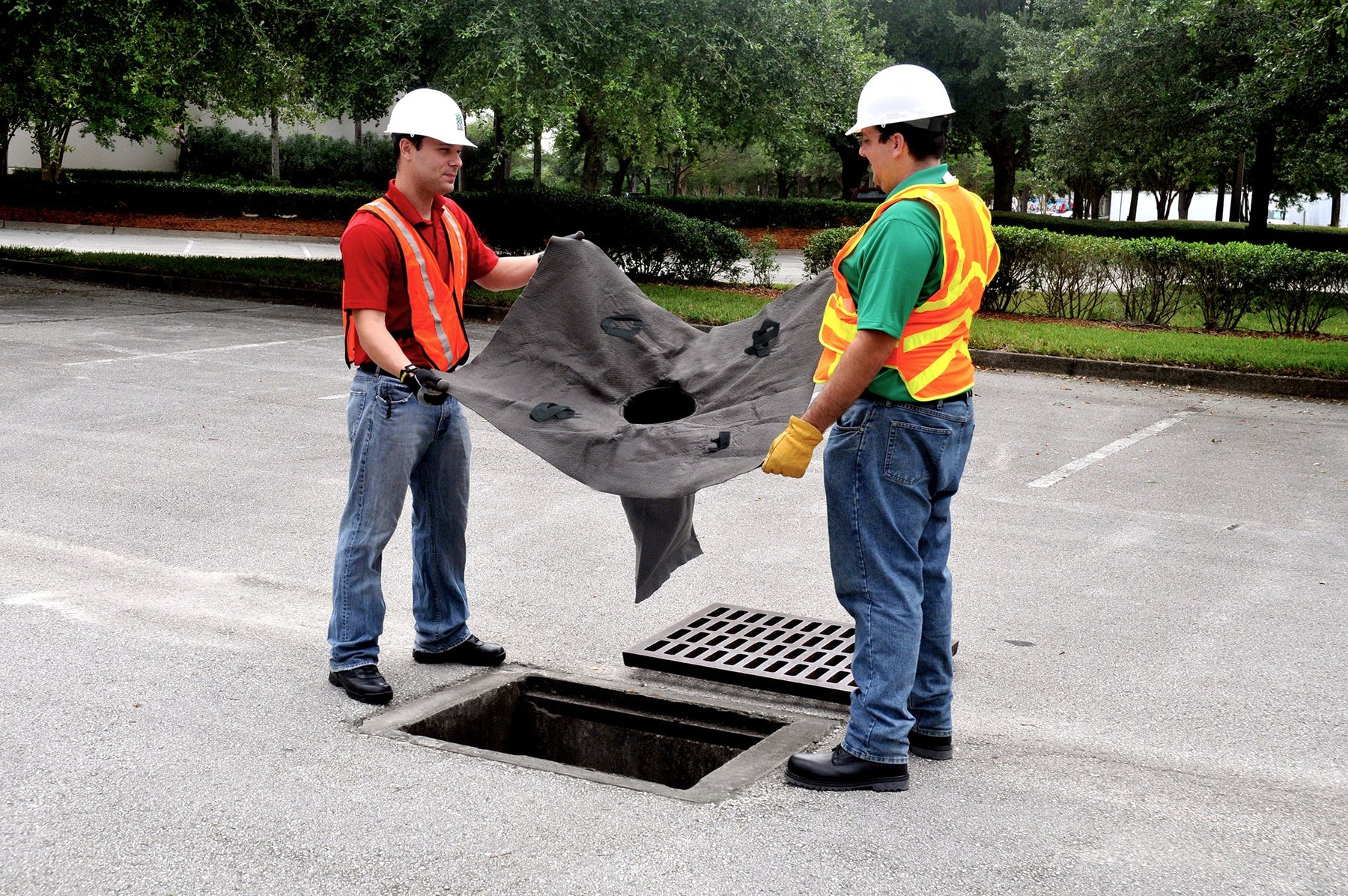Worker installing an UltraTech Oil and Sediment drain guard in a storm drain catch basin
